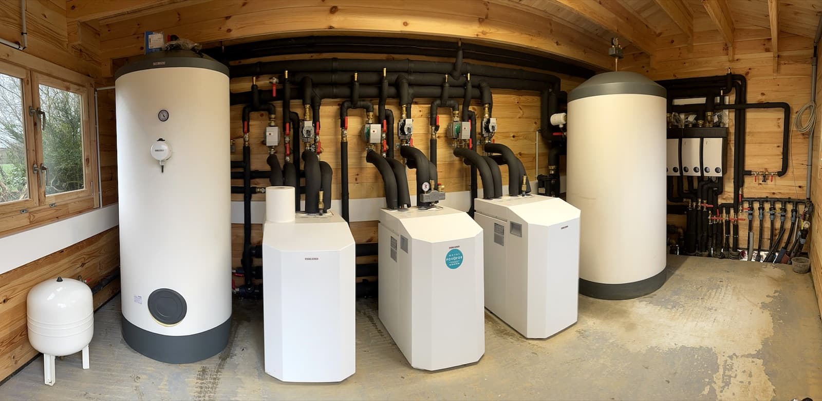 Local technique d'une installation géothermique en bois avec ballons tampon, distributeurs hydrauliques et pompes à chaleur reliées aux sondes enterrées