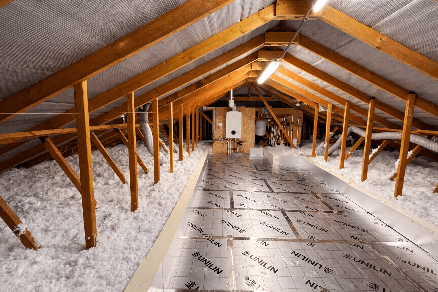Combles perdus isolés par soufflage — plancher recouvert d'isolant blanc et panneau Unilin, charpente bois apparente
