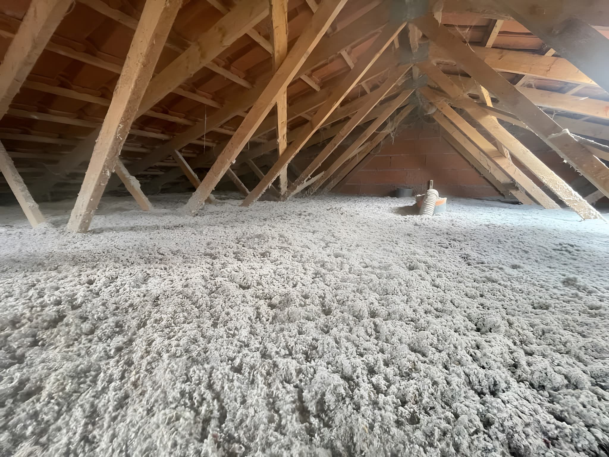 Combles perdus après isolation par soufflage de ouate de cellulose — tapis continu d'isolant gris, charpente en bois