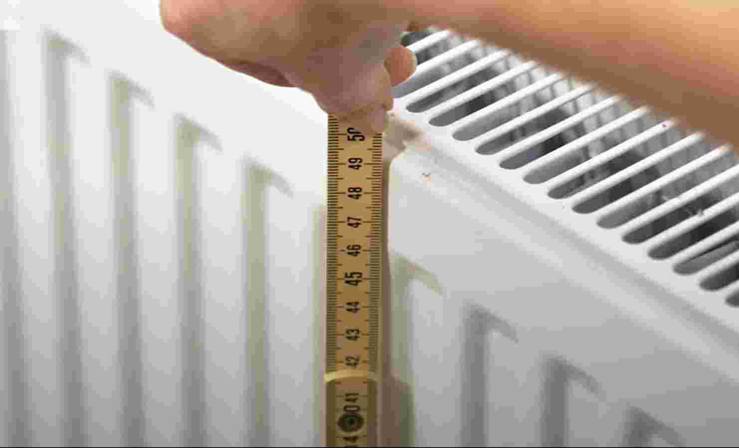 Mètre pliant tenu verticalement contre le côté d'un radiateur à panneaux blanc pour mesurer sa hauteur avant de découper l'isolant