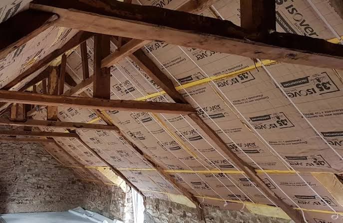 Pose de panneaux isolants entre les chevrons d'une charpente en bois — isolation rampants de toiture par l'intérieur en rénovation
