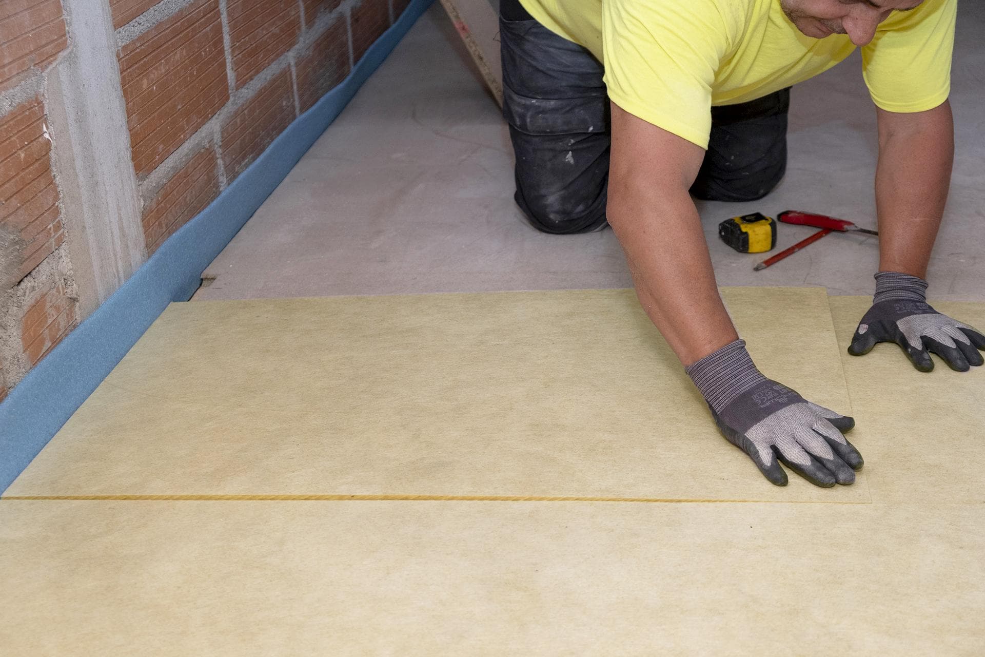 Artisan posant des panneaux isolants rigides sur dalle béton avec bande de désolidarisation bleue — chape sèche isolante pour sol béton