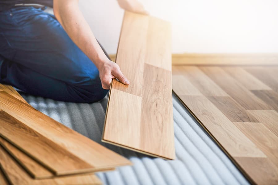 Artisan posant des lames de parquet contrecollé flottant sur sous-couche isolante grise — isolation sol sous parquet en appartement