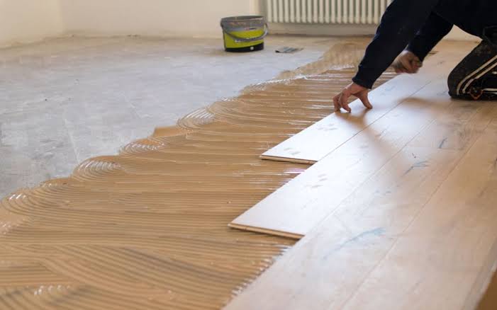Artisan encollant une dalle béton avec colle à parquet en peigne avant pose de lames de parquet massif collé — isolation sol réalisée en amont dans la chape