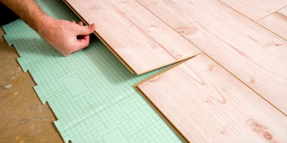 Pose d'une sous-couche isolante verte composite quadrillée sur chape béton avant installation de planches de parquet bois clair