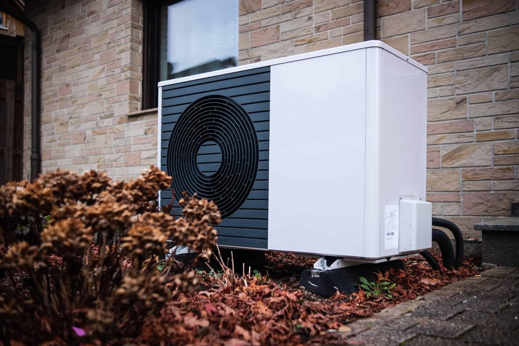 Pompe à chaleur air-eau de grande puissance installée devant une maison en pierre naturelle — feuilles d'automne au sol