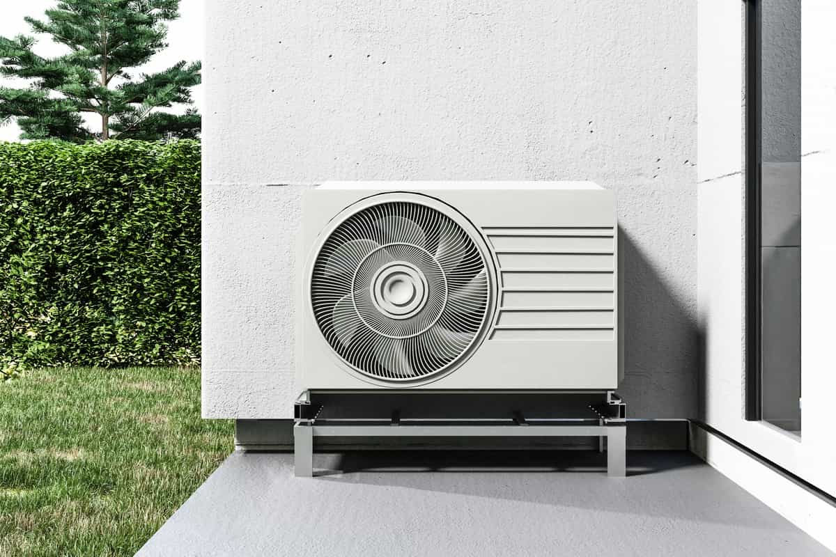Grande pompe à chaleur air-eau sur terrasse béton avec jardin et haies — puissance adaptée grande surface