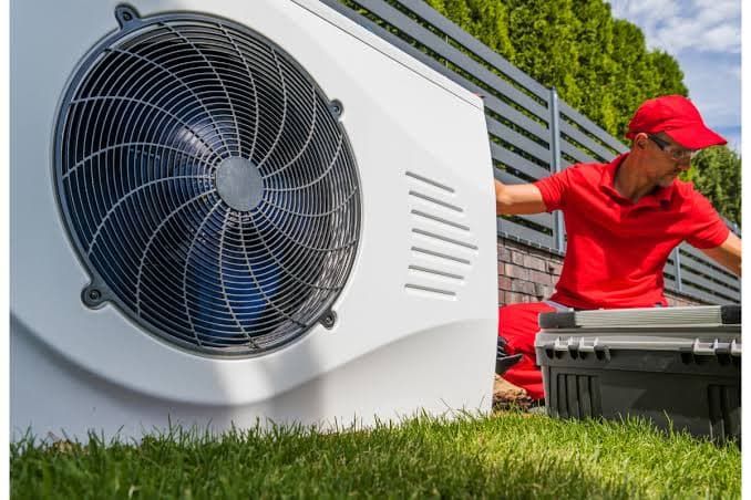 Technicien en uniforme rouge réalisant l'entretien annuel d'une pompe à chaleur air-eau — vérification du circuit frigorifique et nettoyage des échangeurs