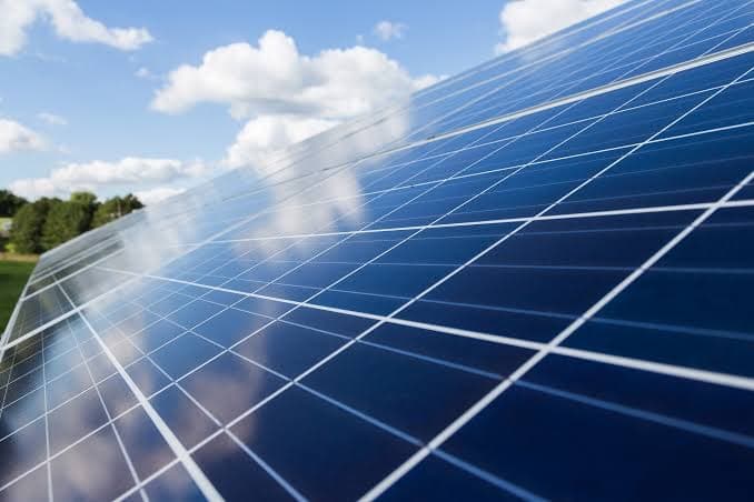 Gros plan sur des modules photovoltaïques monocristallins alignés, dans lesquels se reflètent les nuages d'un ciel bleu d'été