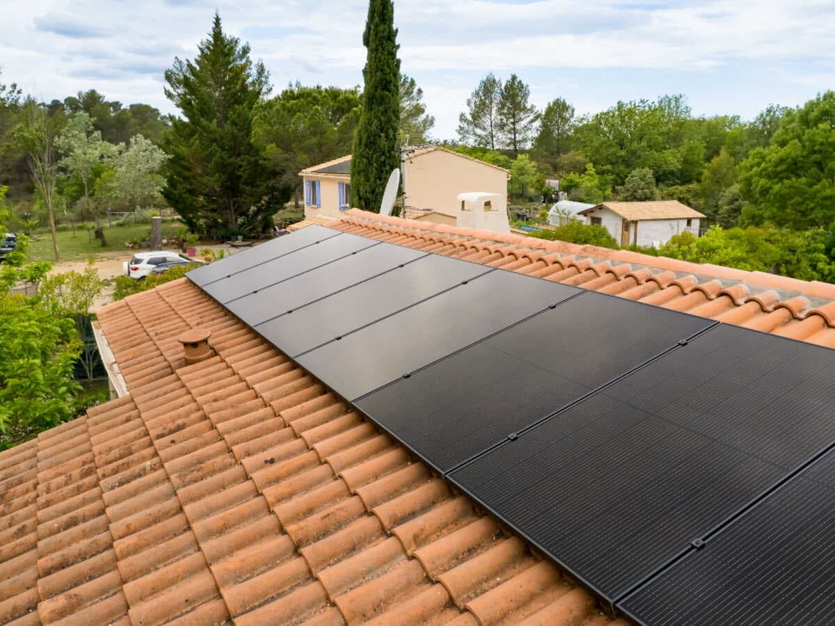 Panneaux solaires noirs posés sur une toiture en tuiles canal d'une maison entourée d'arbres, illustrant les avantages des panneaux solaires pour un particulier