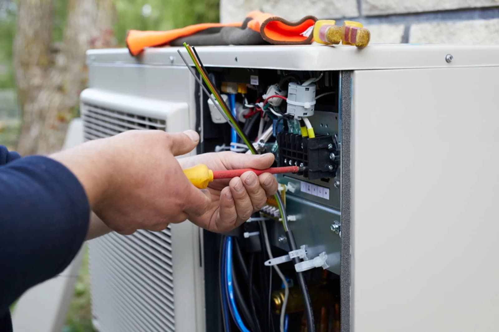 Technicien raccordant les câbles électriques dans le boîtier de commande d'une unité extérieure de pompe à chaleur lors de l'installation