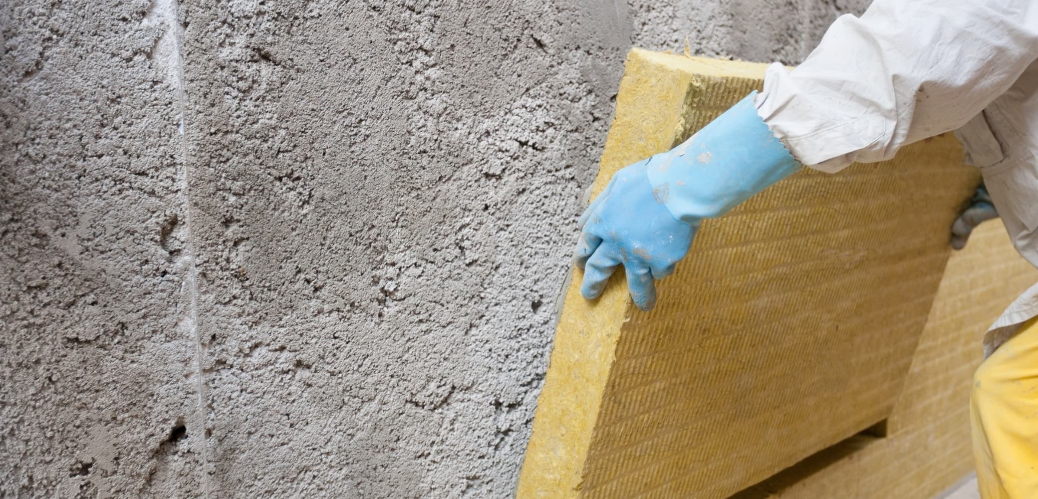 Technicien appliquant de la laine minérale sur un mur brut en pierre pour isoler un mur humide — rénovation thermique par l'intérieur
