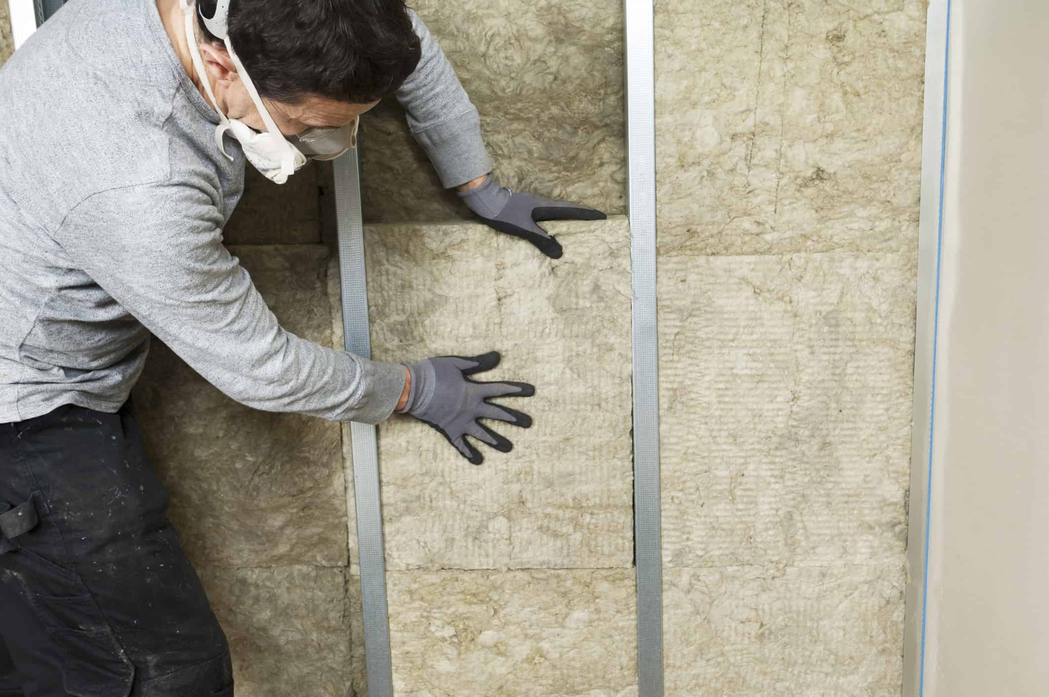 Ouvrier installant de la laine minérale entre les montants métalliques pour l'isolation thermique d'un mur intérieur anciennement humide