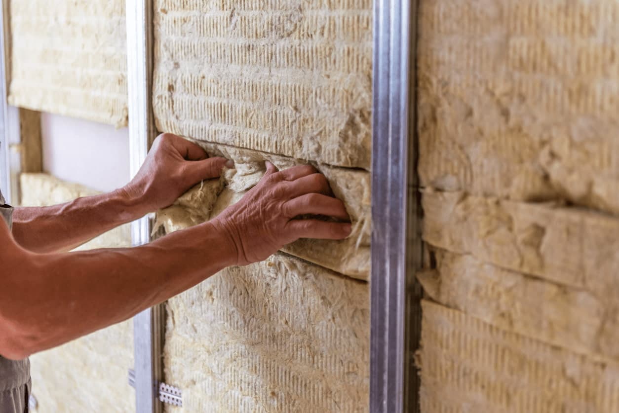 Technicien insérant un panneau de laine de roche entre les montants métalliques d'un doublage mur intérieur
