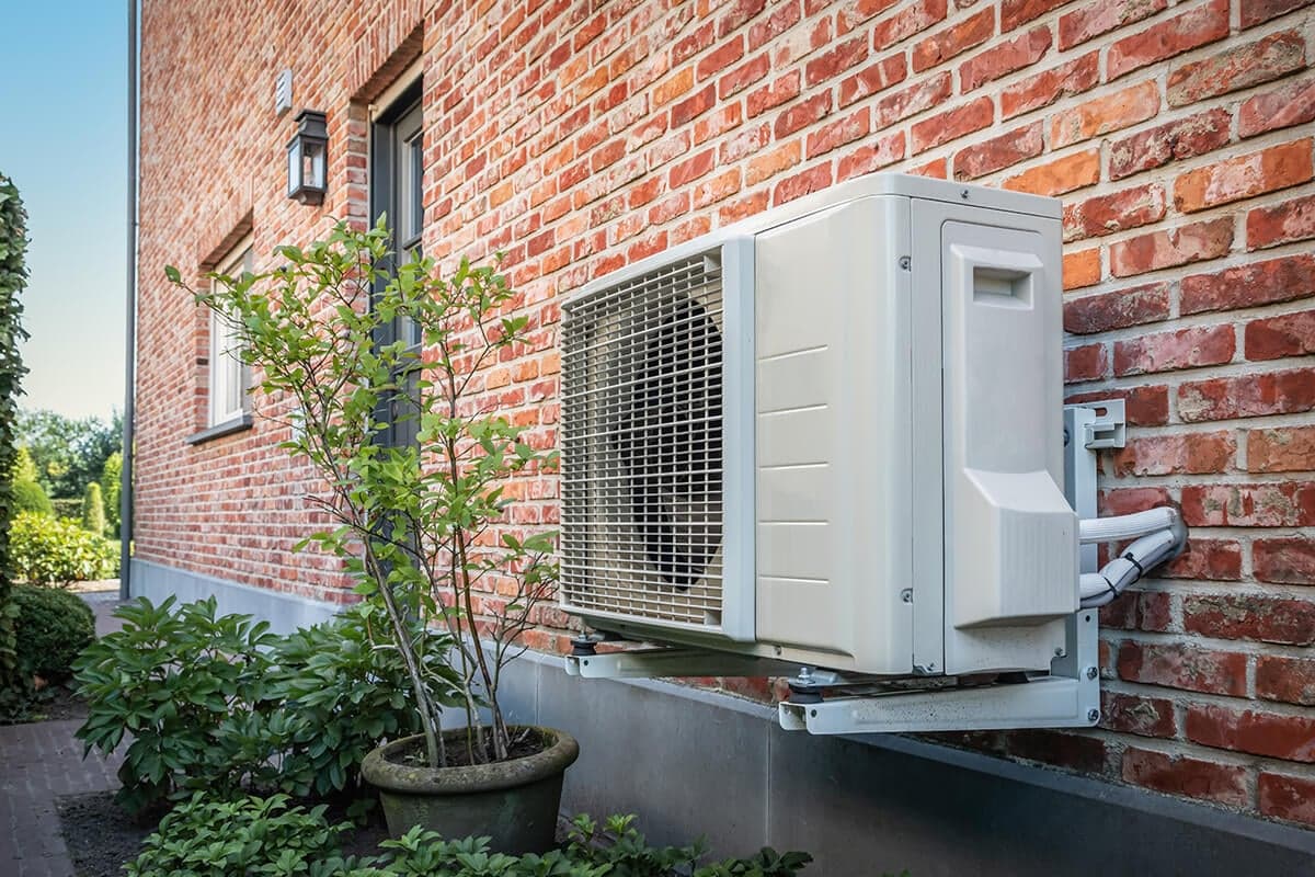 Unité extérieure d'une pompe à chaleur air-eau fixée sur le mur d'une maison en briques rouges avec jardin