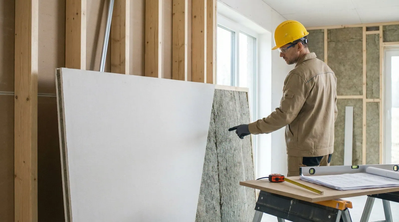 Artisan avec casque jaune examinant une plaque de plâtre isolante et un isolant en laine minérale sur un chantier de rénovation