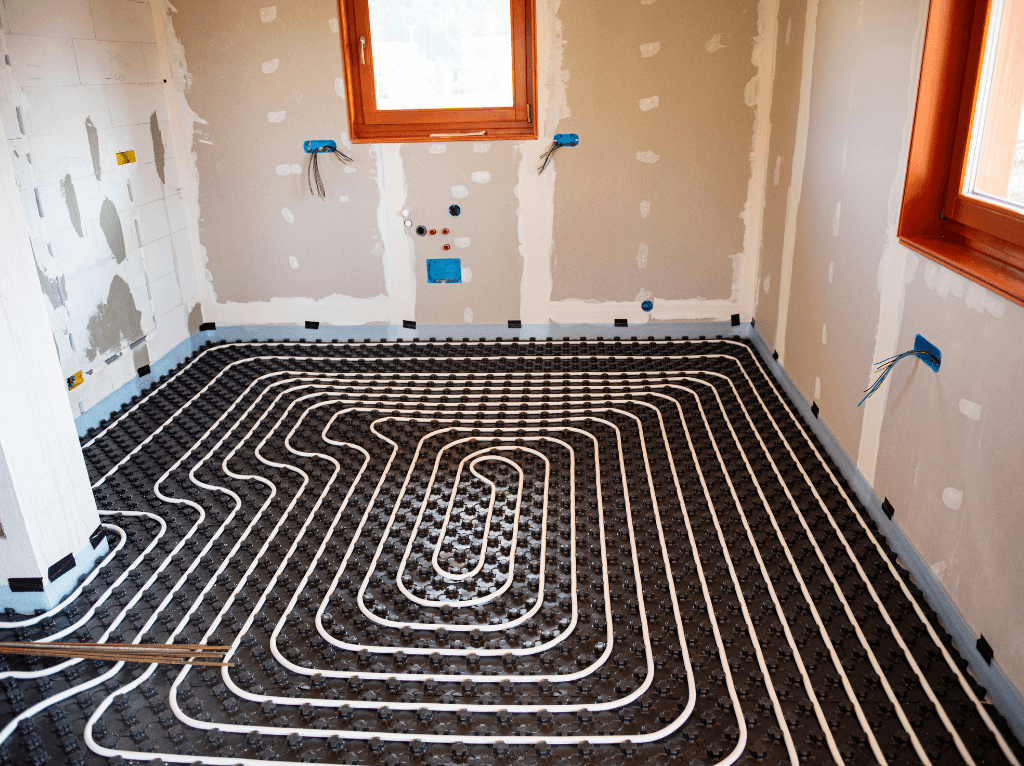 Plancher chauffant hydraulique en cours de pose dans une chambre — tuyaux blancs agrafés sur plaque isolante noire avant chape