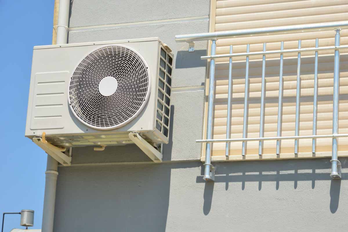 Unité extérieure d'une pompe à chaleur fixée sur un support mural en façade, à côté d'un balcon avec store, en appartement