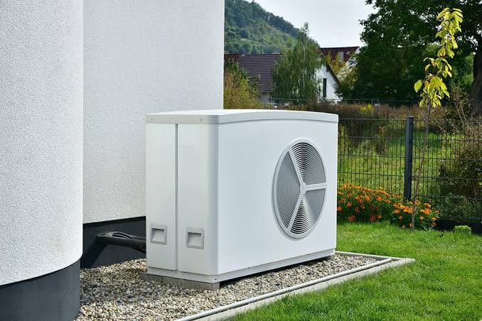 Unité extérieure blanche d'une pompe à chaleur air-eau posée sur lit de gravier dans un jardin, illustrant la question du bruit d'une pompe à chaleur
