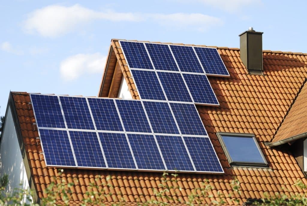 Maison à deux pans de toiture en tuiles orangées couverts de panneaux solaires bleus, l'un de 14 modules et l'autre de 8 modules, illustrant la taille des panneaux solaires sur un toit
